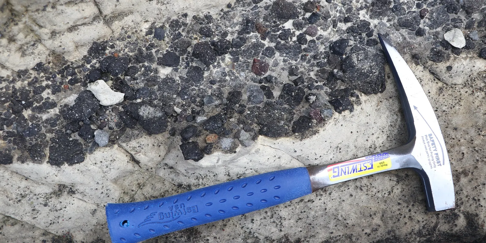 Geologenhammer liegt als Maßstab auf einer Gesteinsschicht